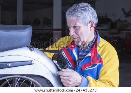 middle aged mechanic is adjusting the registration plate of a classic motorcycle in process of restoration at his workshop - focus on the man face
