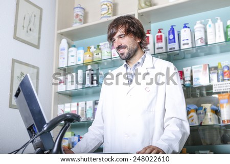 smiling young male pharmacist using the computer at the pharmacy standing looking at the screen - focus on the face