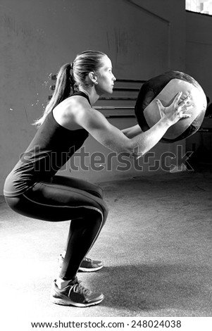 profile of a young female athlete crouched doing wall balls exercises at the gym - focus on the woman face