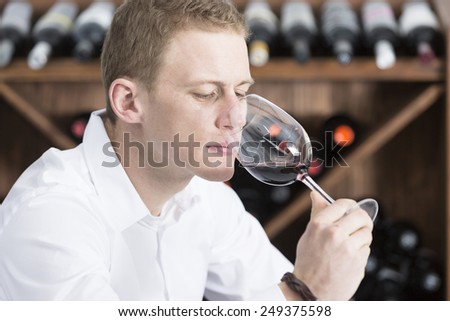 young man on a wine tasting session on the olfactory phase is analyzing the red wine with the wineglass in the nose at a restaurant - focus on the man face