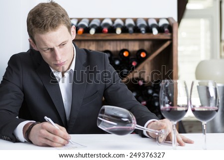 man on a wine tasting session on the visual phase is writing down in a wine tasting sheet at a restaurant - focus on the man face