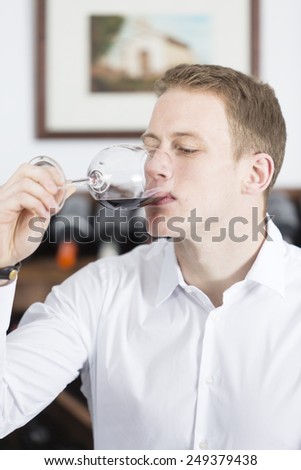 young man on a wine tasting session on the gustatory phase is tasting the red wine at a restaurant - focus on the man face