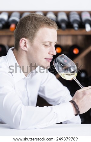 young man on a wine tasting session on the olfactory phase is analyzing the white wine smelling the wineglass at a restaurant - focus on the man face
