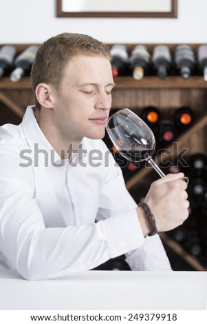 young man on a wine tasting session on the olfactory phase is analyzing the wine smelling the wineglass at a restaurant - focus on the man face