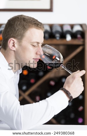 young man on a wine tasting session on the olfactory phase is analyzing the wine with the wine glass in the nose at a restaurant focus on the man face