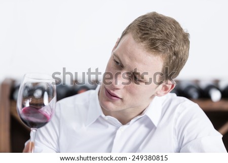 young man on a wine tasting session on the olfactory phase is analyzing the red wine shaking the glass of wine at a restaurant - focus on the man face