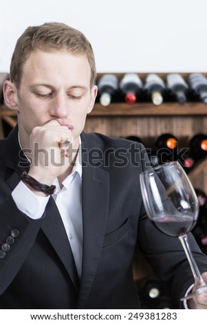 thoughtful young man is evaluating a red wine on a wine tasting session holding a red wine glass at a restaurant - focus on the man face