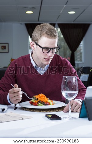 young businessman eating a salad while is working with a tablet at a restaurant - focus on the man face