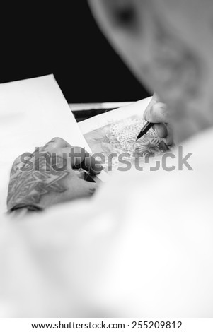 tattoo artist is drawing the design of a leopard on a paper sheet at his tattoo shop - focus on the leopard eye