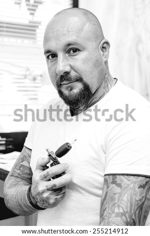 portrait of a tattoo artist holding a tattoo machine in the tattoo cabin at his tattoo shop - focus on the man face