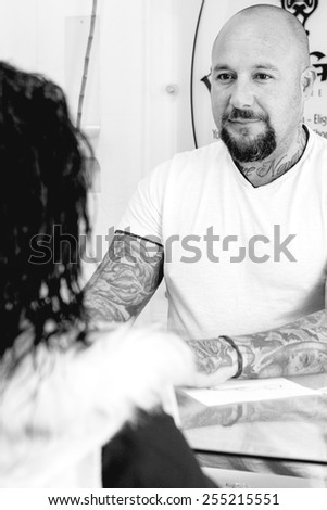 young male tattoo artist is attending to a young female customer before the tattoo session at the tattoo shop - focus on the man face