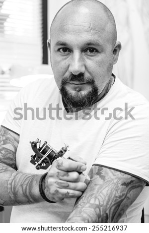 portrait of a tattoo artist is tattooing his arm in the tattoo cabin at his tattoo shop - focus on the man face