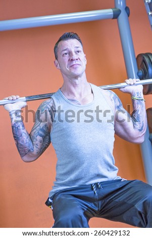 young man making barbell squat - leg exercise - at the gym - finish exercise - focus on the man face