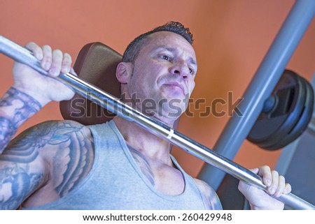 closeup of a man making seated barbell military press - dorsal exercise - at the gym - start exercise - focus on the man face