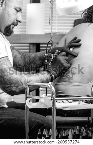 tattooist is tattooing the back of a young woman in the tattoo cabin at his tattoo shop - focus on the tattoo machine
