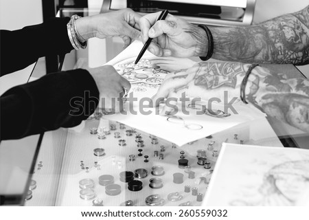 detail of a tattoo design of a tattoo artist is showing to a young female customer the tattoo design before the tattoo session at the tattoo shop - focus on the tip of the pen