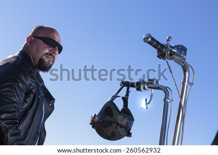 portrait of a chopper motorcyclist rider sitting on his motorcycle with the sun reflected on the rear view mirror at sunrise - focus on the face