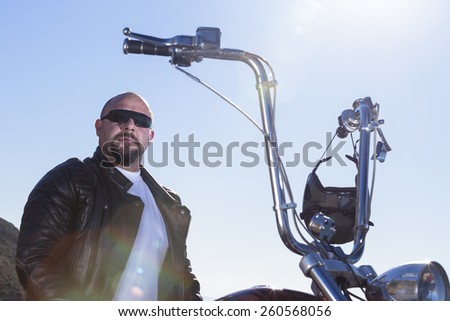 portrait of a chopper motorcycle rider sitting on his motorcycle looking at the camera - focus on the face - flare on the jacket