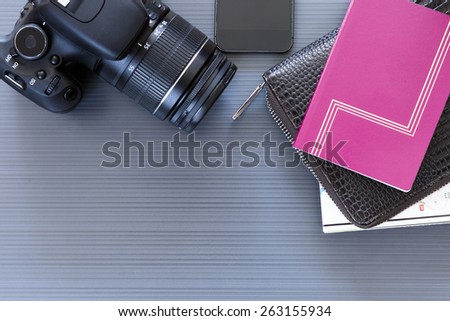 top view of a desktop with a travel stuff consisting on a camera, a passport, a documents case, a phone and a map on a desk background - suitable for copy space