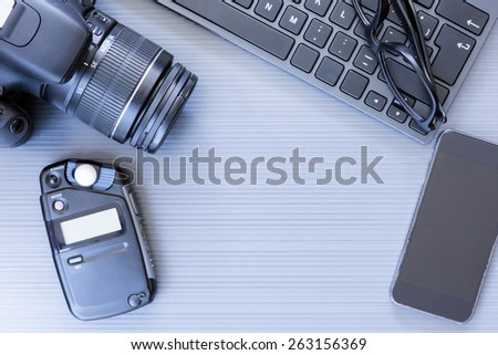 top view of a desktop of a photographer consisting on a camera, a keyboard, a photometer, a smart phone and a reading glasses on a grey desk background - suitable for copy space