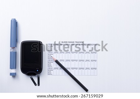 top view of a diabetes control set background consisting of: an insulin pen, a glucometer, test strips, a blood glucose diary and a pen on a white background