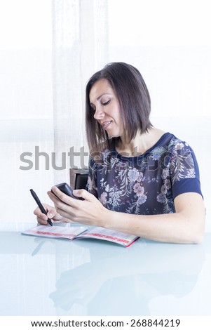 young woman is writing the data on a blood glucose diary after scanning the sensor of the glucose monitoring system with a reader at home - focus on the woman left eye