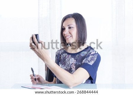 smiling young woman is looking at a reader after scanning the sensor of the glucose monitoring system ready to write the value on a blood glucose diary at home - focus on the woman face