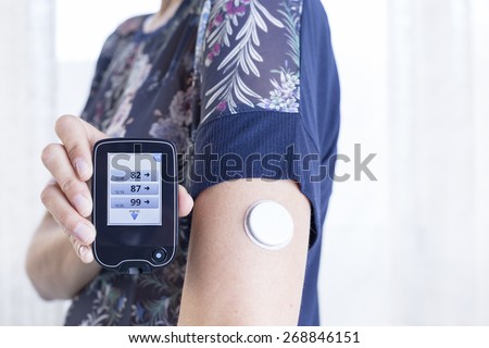 closeup of a hand of a young woman showing the reader after scanning the sensor of the glucose monitoring system - focus on the reader