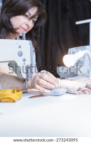 young dressmaker is pinning the fabric seated on a sewing machine at her sewing atelier - focus on her right middle finger