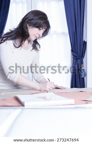 female tailor is drawing a pattern with a pencil with a sketchbook on the table at her sewing atelier - focus on the face