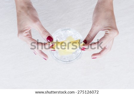 top view of the hands of a woman decorating a gin tonic balloon glass with a curled lemon peel on a gin tonic preparation session - focus on the curled lemon peel
