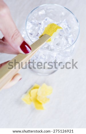 hand of a woman holding a lemon peel with  a bamboo ice tongs on a flavoring process of a gin tonic on a gin tonic preparation session - focus on the lemon peel