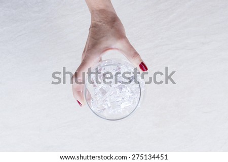top view of a woman hand holding a balloon glass full of ice cubes on the glass chilling process on a gin tonic preparation session - focus on the ice cubes