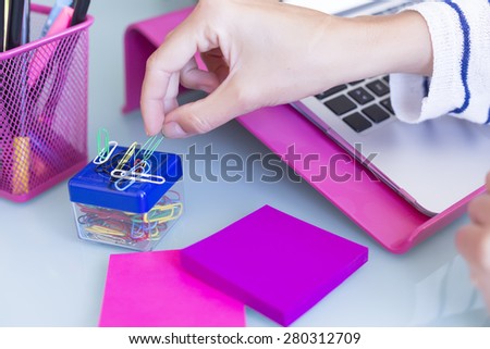 detail of the hand of a woman taking a paperclip on a working desk - focus on the thumb