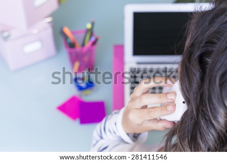 rear view of a woman speaking on a mobile phone while is working on a working desk - focus on the middle finger