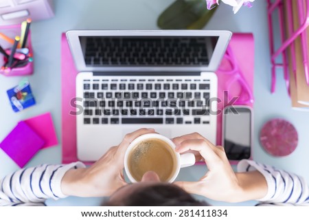 top view of a woman drinking a cup of coffee on a working desk  - focus on the cup of coffee