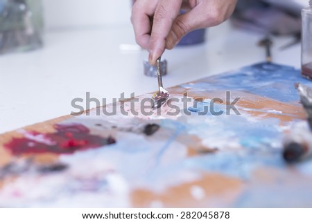 detail of the hand of a male painter mixing paint with the palette knife over the palette at his painting studio - focus on palette knife
