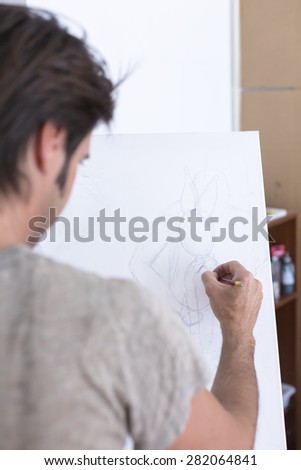 back view of a man drawing with a pencil on canvas at his painting studio - focus on the drawing