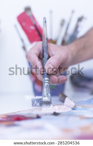 closeup of the hand of a male painter taking paint with a paintbrush from the palette - focus on the paintbrush