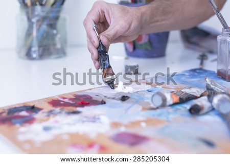 detail of the hand of a male painter adding paint to the palette at his painting studio - focus on paint