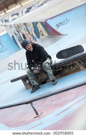 portrait of a smiling old man skater is sitting on a bench on a skating park - focus on the face