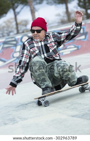 old man skater is skating crouched with his skateboard on a skating park - focus on the face