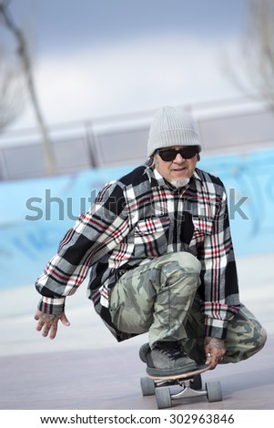 closeup of an old man skater is skating crouched with his skateboard on a skating park - focus on the face