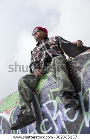 bottom view of an old man skater sitting on a skate park holding his skateboard - focus on the face