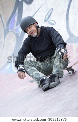 portrait of an old man skater is sitting on his skateboard on a skating park - focus on the face