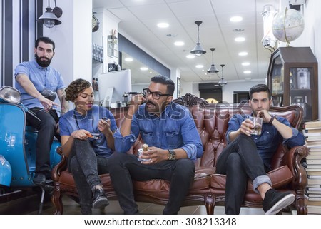 portrait of a hairstylist with his staff sitting on a couch on their break time at his barber shop - focus on the barber face