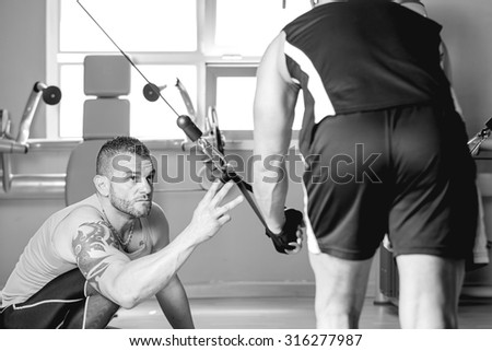 personal trainer helping young man making dorsal exercise - at the gym - focus on the trainer right eye