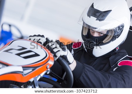 closeup of a concentrated karting pilot sitting on his go-kart before starting a race in an outdoor go karting circuit - focus on the left eye
