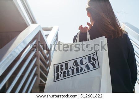 Rear view of incognito brunette holding Black Friday shopping bag while standing outdoors. Copy space