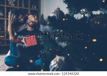 Young couple interchanging gifts on Christmas eve nearby decorated fir tree.